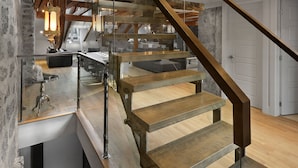 Un interior moderno con escalera de madera, barandales de vidrio y paredes de ladrillo visto.