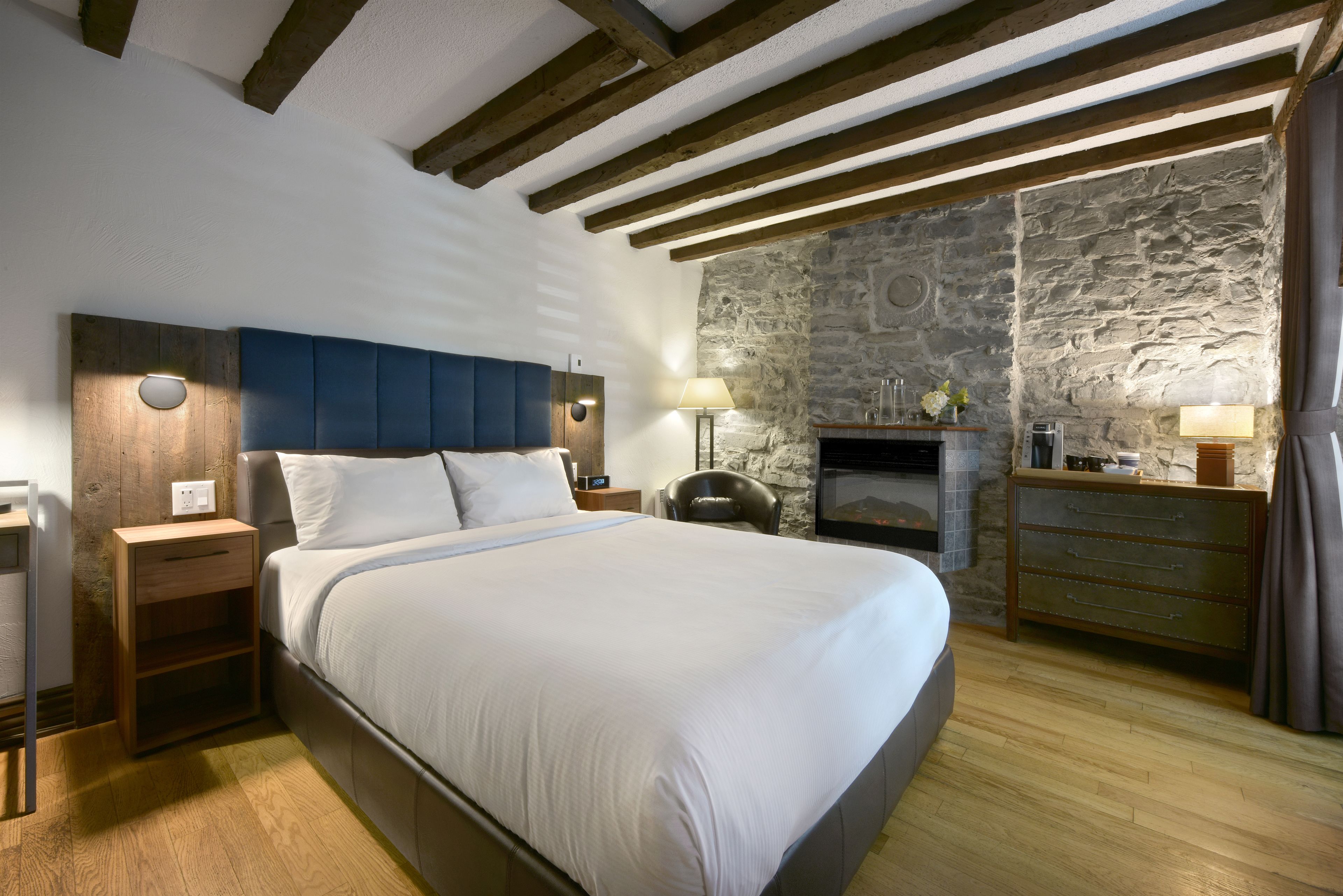 A bedroom with a large bed, wooden headboard, stone wall, and a fireplace.