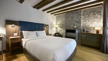 A bedroom with a large bed, wooden headboard, stone wall, and a fireplace.