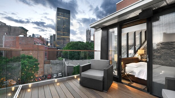 Un balcón moderno con una silla de mimbre, un ventanal de vidrio que da a un dormitorio y vistas a la ciudad.
