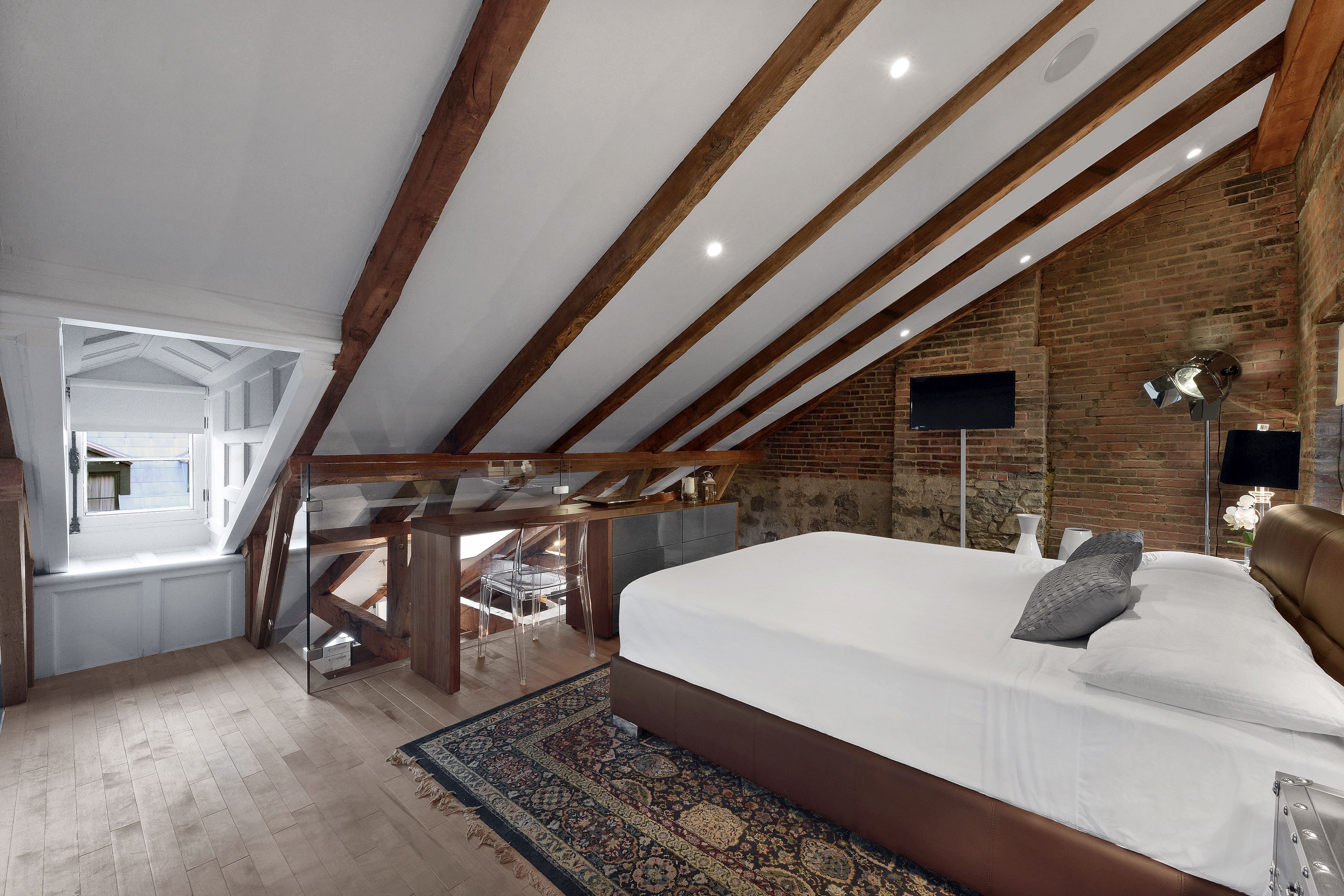Une chambre avec un grand lit, des poutres en bois, un mur en briques et un téléviseur fixé au mur.