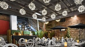 Un comedor interior con mesas y sillas, iluminación decorativa en el techo y una pared de ladrillo.