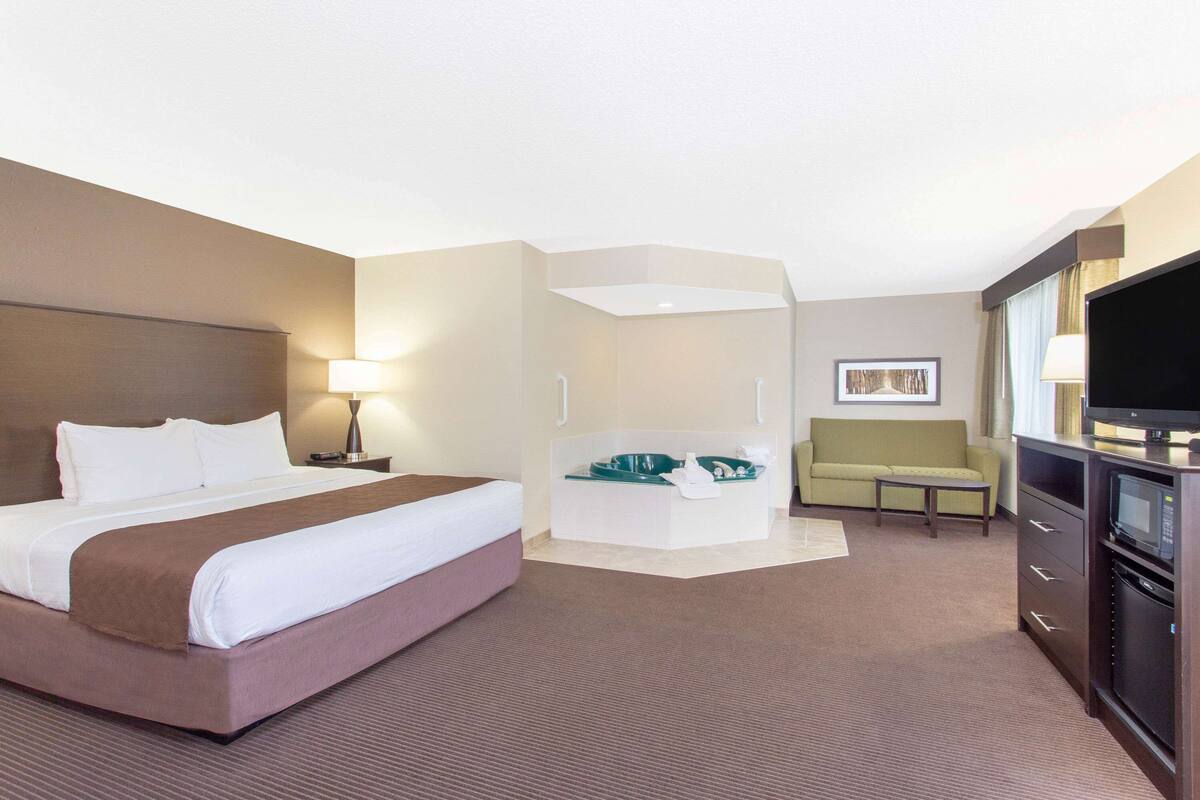 A hotel room with a large bed, a small sofa, a desk, a TV, and a bathroom area.