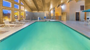 Une piscine intérieure à l’eau d’un bleu cristallin, avec des poutres en bois au plafond et des chaises longues disposées le long des bords.