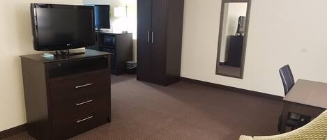 Ein Hotelzimmer mit einem Flachbildfernseher auf einer Kommode, einem hohen Kleiderschrank, einem kleinen Tisch und einem Spiegel an der Wand.