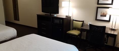 A hotel room with two beds, a TV, a desk with a chair, and a lamp.