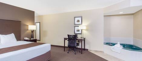 A hotel room with a large bed, a desk with a chair, a desk lamp, a telephone, and a bathtub.