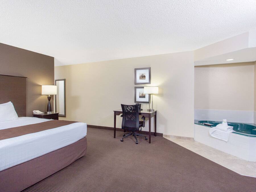 Habitación de hotel con una cama grande, un escritorio con silla, una lámpara de escritorio, un teléfono y una bañera.