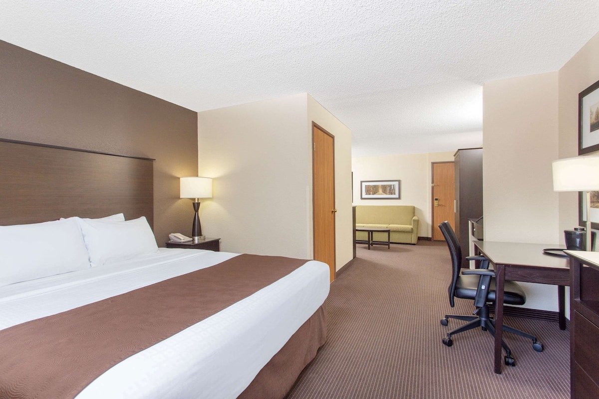A hotel room with a large bed, a desk, a chair, a lamp, and a small table.