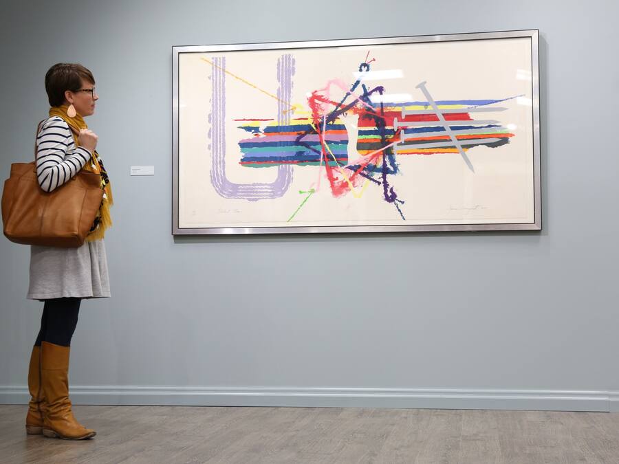 Une personne se tient devant un tableau abstrait encadré dans une galerie d’art.