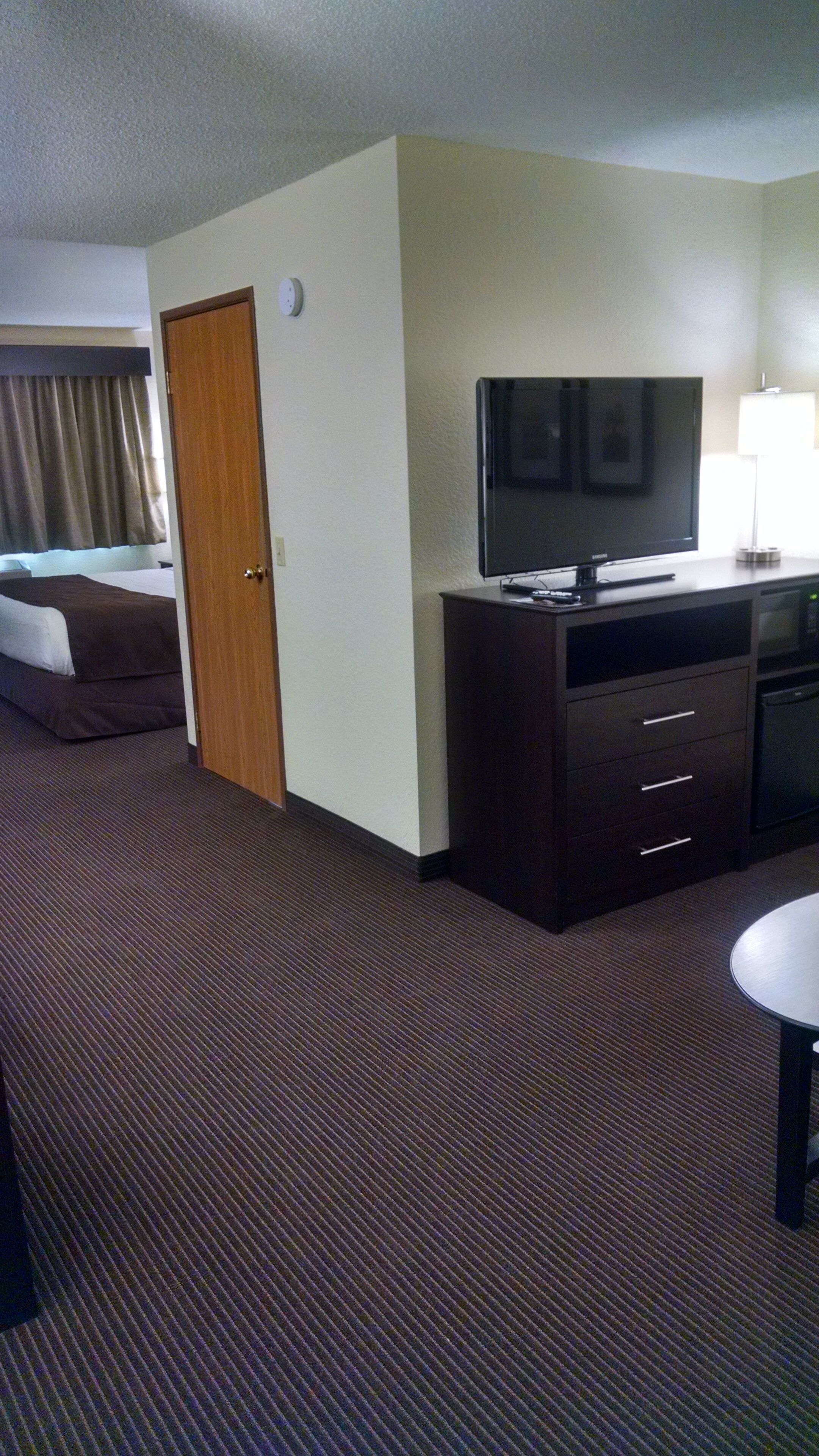 Una habitación de hotel con una cama, un televisor en un mueble bajo, un escritorio con una lámpara y un microondas.