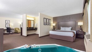 A hotel room with a large bed, a desk, a chair, a bathroom with a bathtub, and a desk lamp.