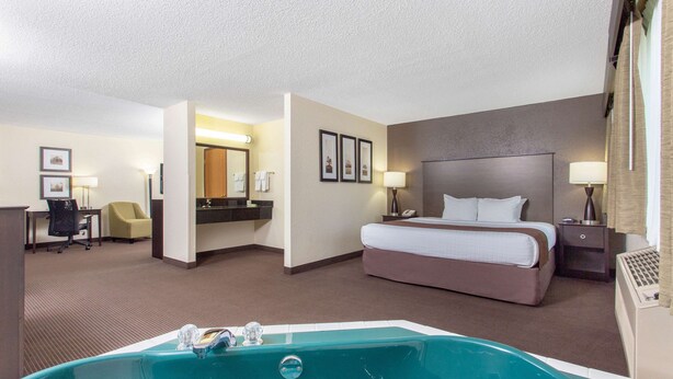 Une chambre d’hôtel avec un grand lit, un bureau, une chaise, une salle de bain avec baignoire et une lampe de bureau.