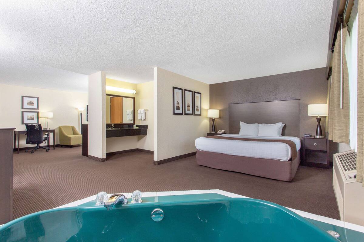 A hotel room with a large bed, a desk, a chair, a bathroom with a bathtub, and a desk lamp.