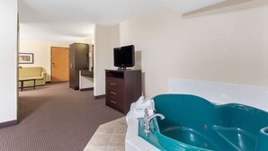 Une salle de bain d’hôtel avec une grande baignoire, un téléviseur posé sur un meuble et un couloir menant à une chambre.