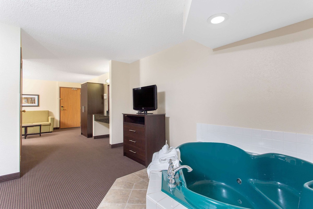 A hotel bathroom with a large bathtub, a television on a cabinet, and a hallway leading to a room.
