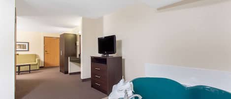 Ein Hotelbad mit einer großen Badewanne, einem Fernseher auf einem Schrank und einem Flur, der in ein Zimmer führt.