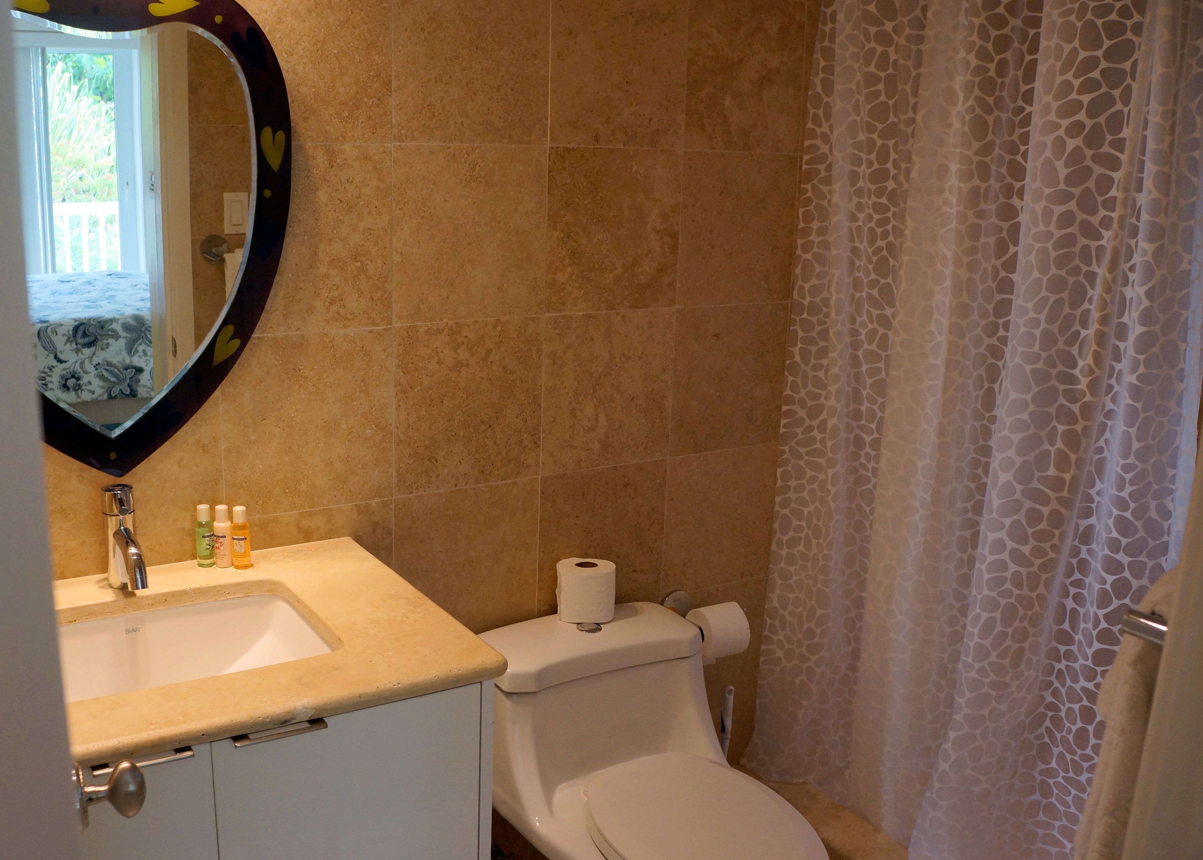 Une salle de bain avec un mur recouvert de carreaux beiges, un lavabo blanc avec un miroir, des articles de toilette et des toilettes.