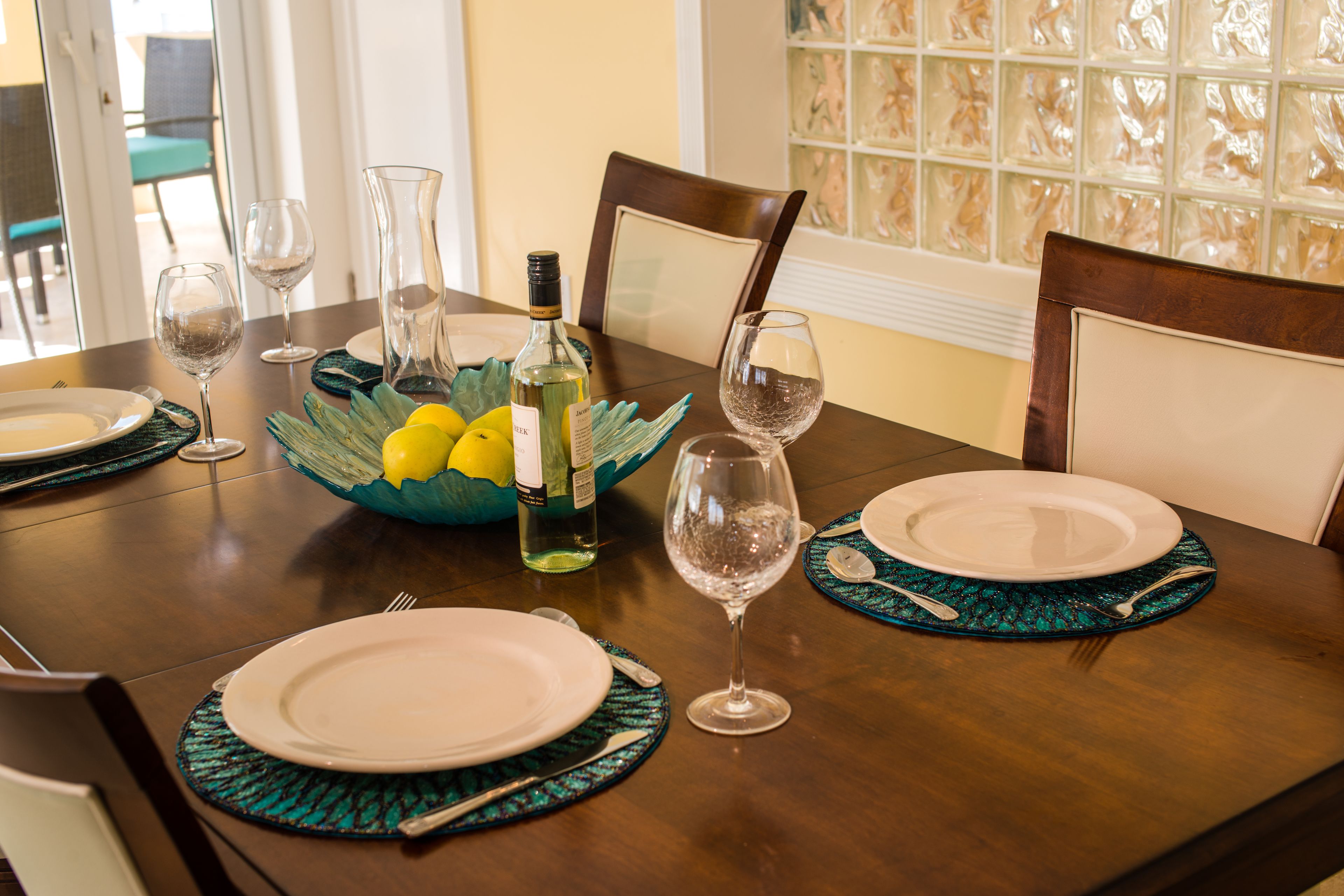 Une table à manger dressée avec des assiettes, des couverts et des verres à vin, ainsi qu'un bol de citrons et une bouteille de vin.