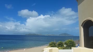 Une vue sur la plage, avec un ciel dégagé, une côte sablonneuse et des îles à l’horizon.