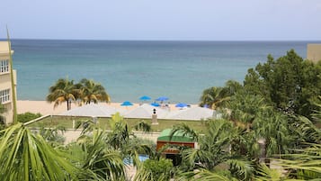 Vista de un resort frente a la playa, con piscina, sombrillas y palmeras.