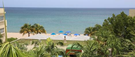 A view of a beach resort with a pool, umbrellas, and palm trees.
