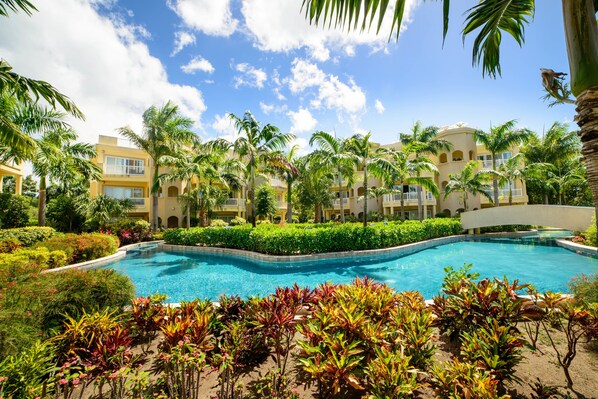 A resort with a central swimming pool, surrounded by lush greenery and palm trees.