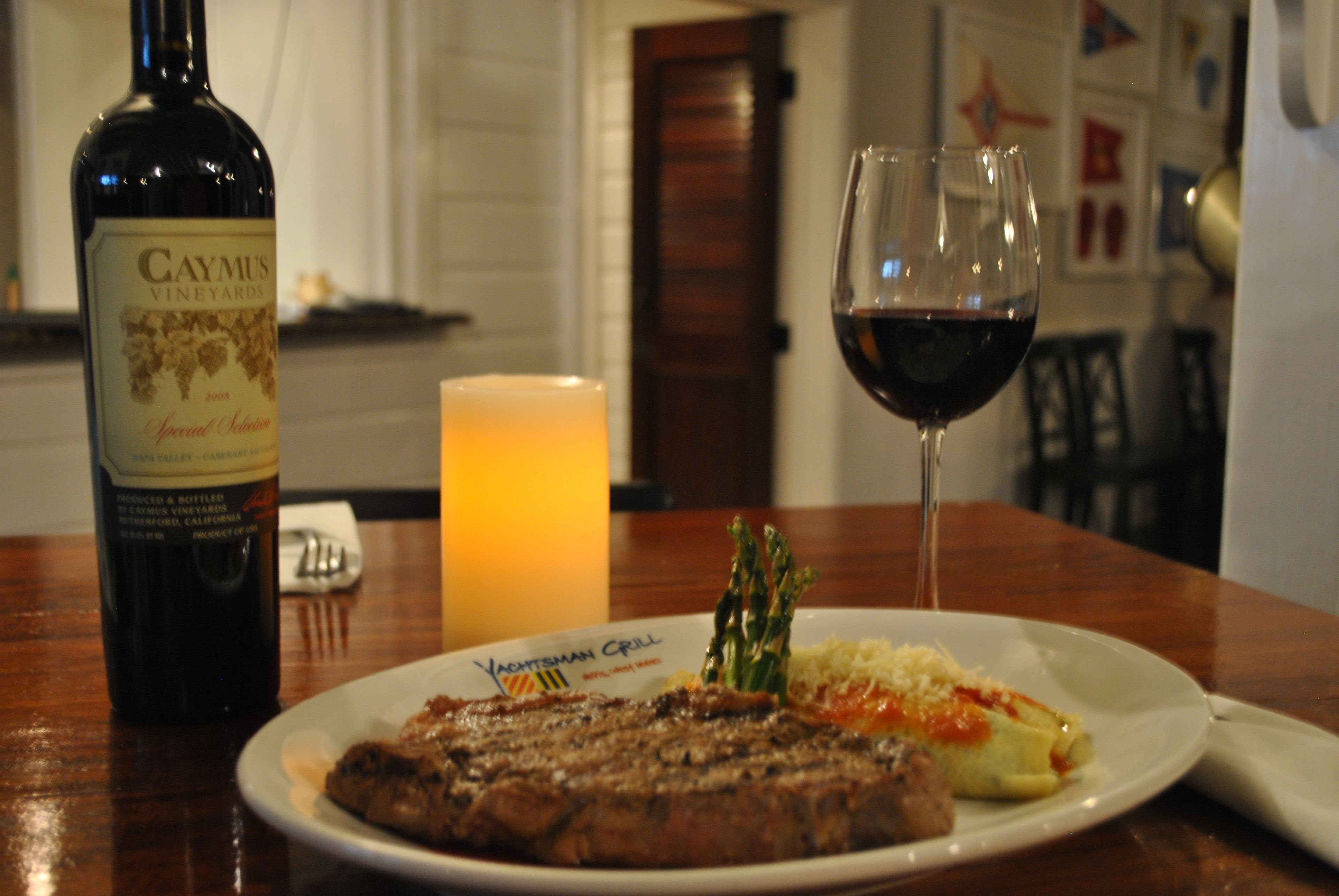 A plate of steak with asparagus and a glass of red wine on a wooden table.