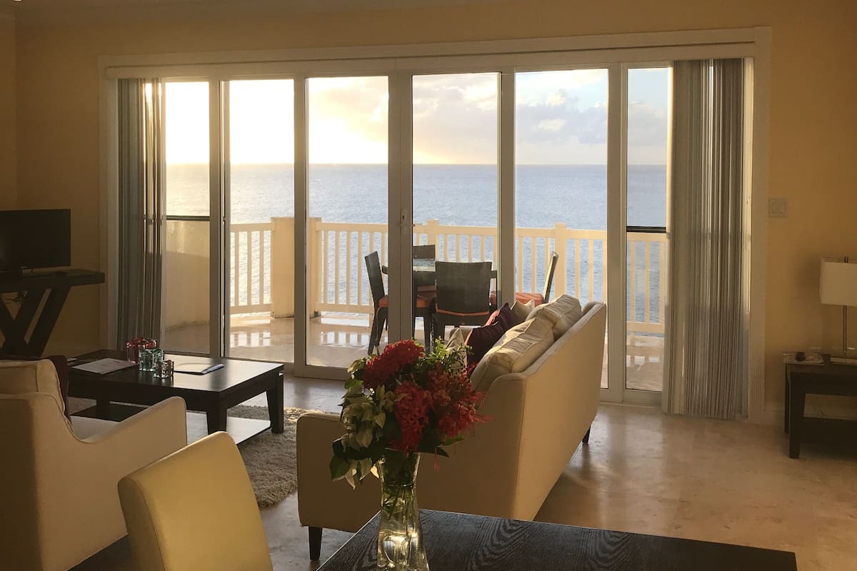 Een ruime woonkamer met een grote schuifpui die leidt naar een balkon met uitzicht op zee.