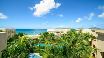 Guests can enjoy ocean views from their balcony, with the pool area surrounded by lush greenery nearby.