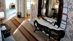 Una habitación con papel tapiz floral, un espejo sobre un tocador, un cuenco rojo sobre una mesa y una alfombra estampada en rojo y beige.