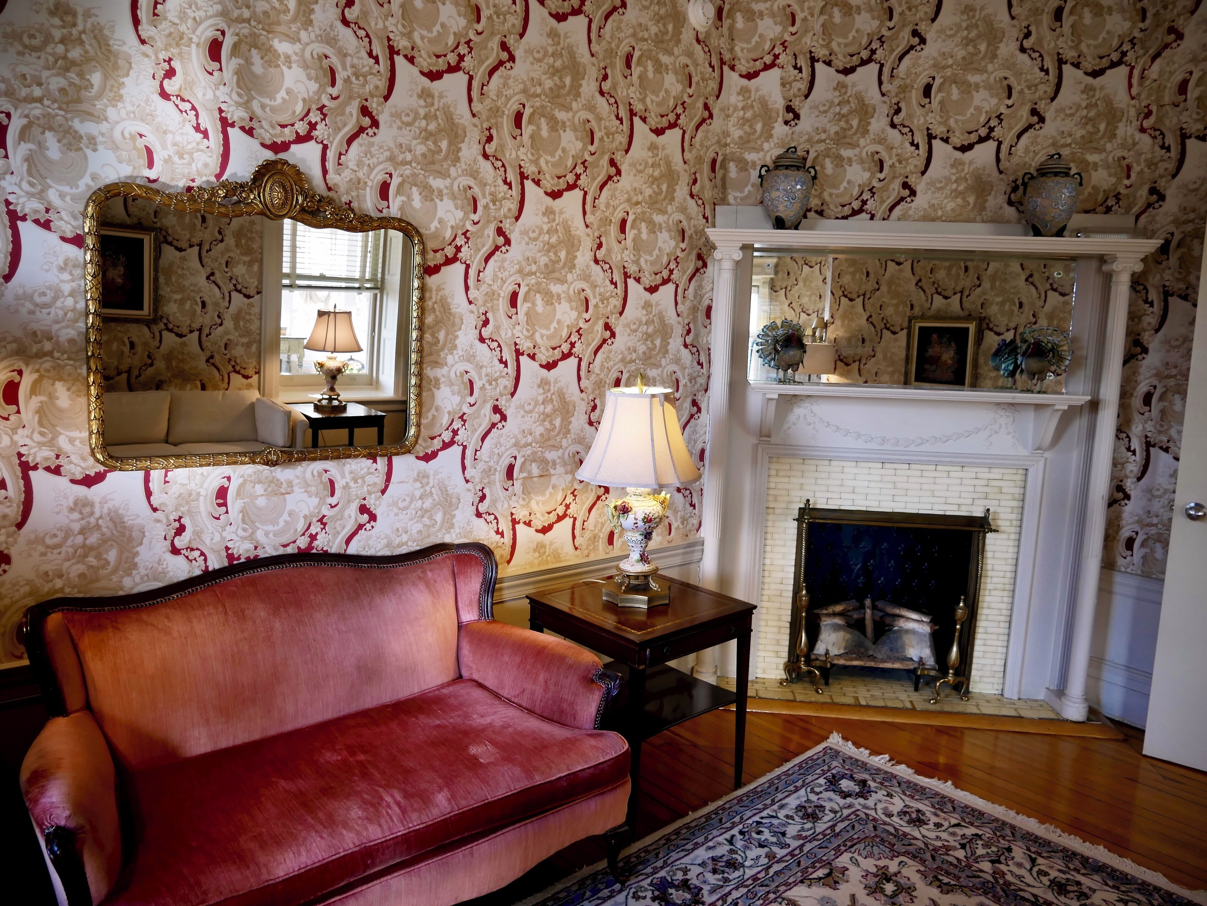 A room with a red sofa, a mirror, a lamp, and a fireplace with decorative items.