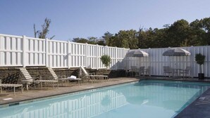 A swimming pool with lounge chairs and umbrellas, surrounded by a white fence and stone wall.