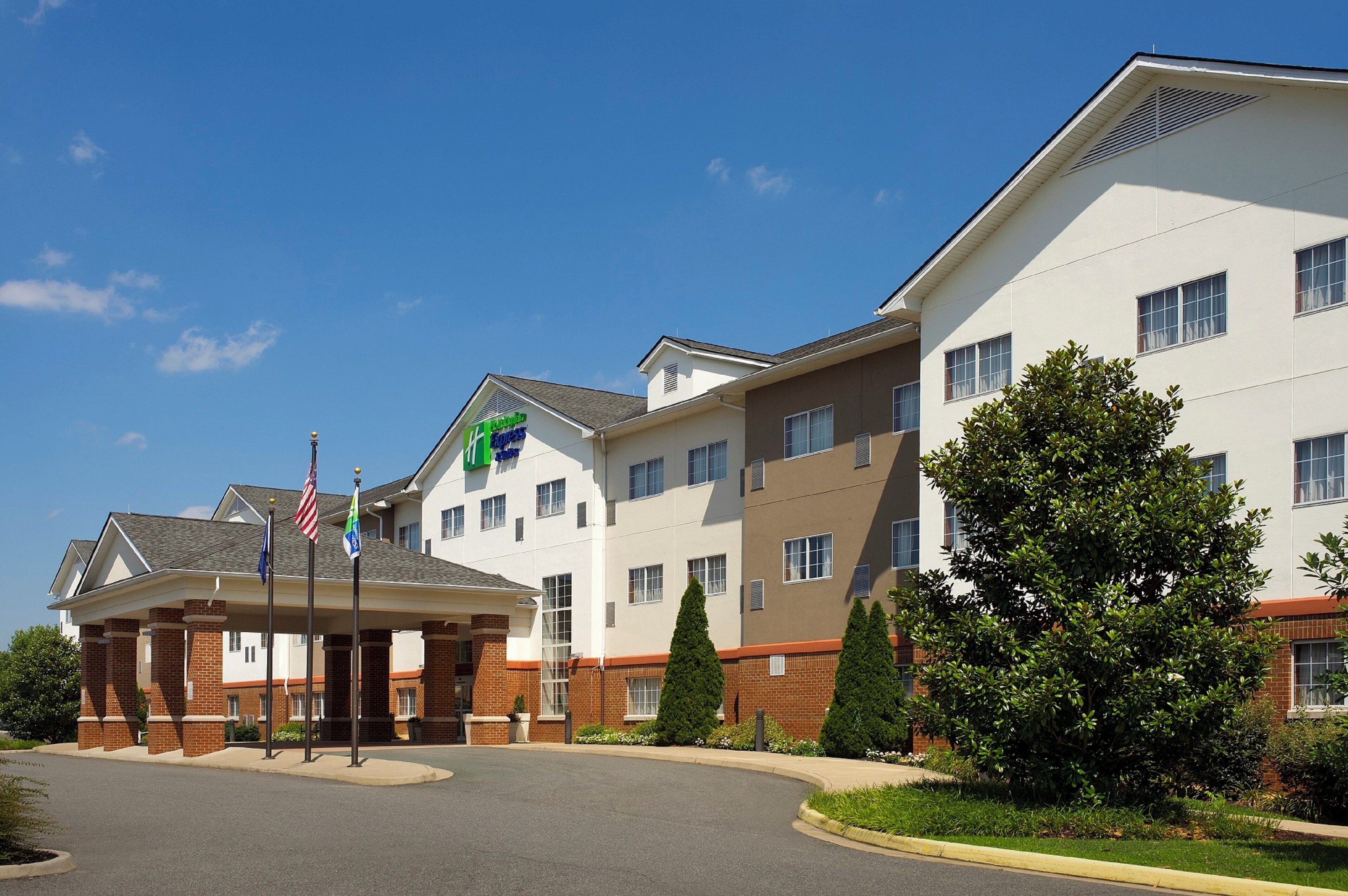 A multi-story hotel with a central entrance, flagpoles, and a landscaped area with trees.