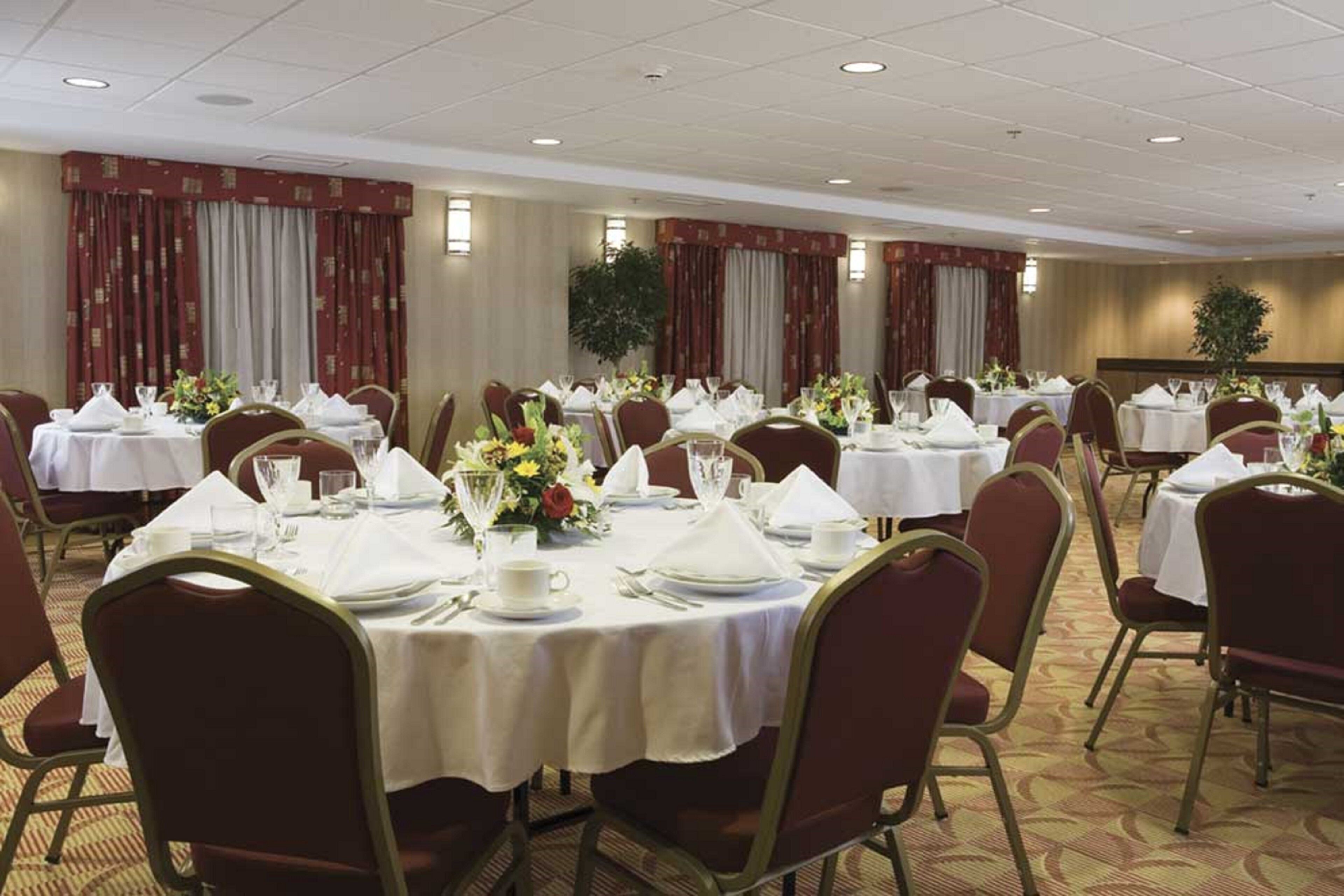A banquet hall with round tables set for dining, each with white tablecloths and floral centerpieces.