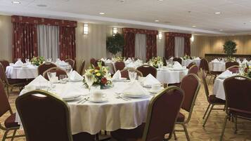 A banquet hall with round tables set for dining, each with white tablecloths and floral centerpieces.