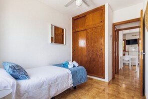 A bedroom with two beds, a wooden wardrobe, a mirror, and a view into the kitchen. - Apartamentos Mar Blanca (Ciutadella de Menorca)