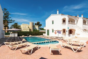 A pool area with lounge chairs, a stone tower, and a white building with balconies.