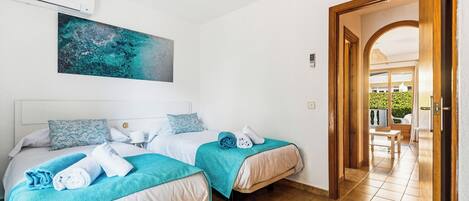 Habitación de hotel con dos camas, ventilador de techo, un cuadro y vista al área exterior.