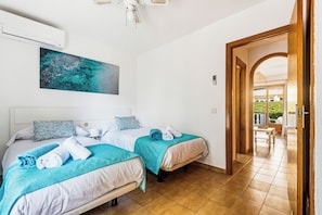 Habitación de hotel con dos camas, ventilador de techo, un cuadro y vista al área exterior.