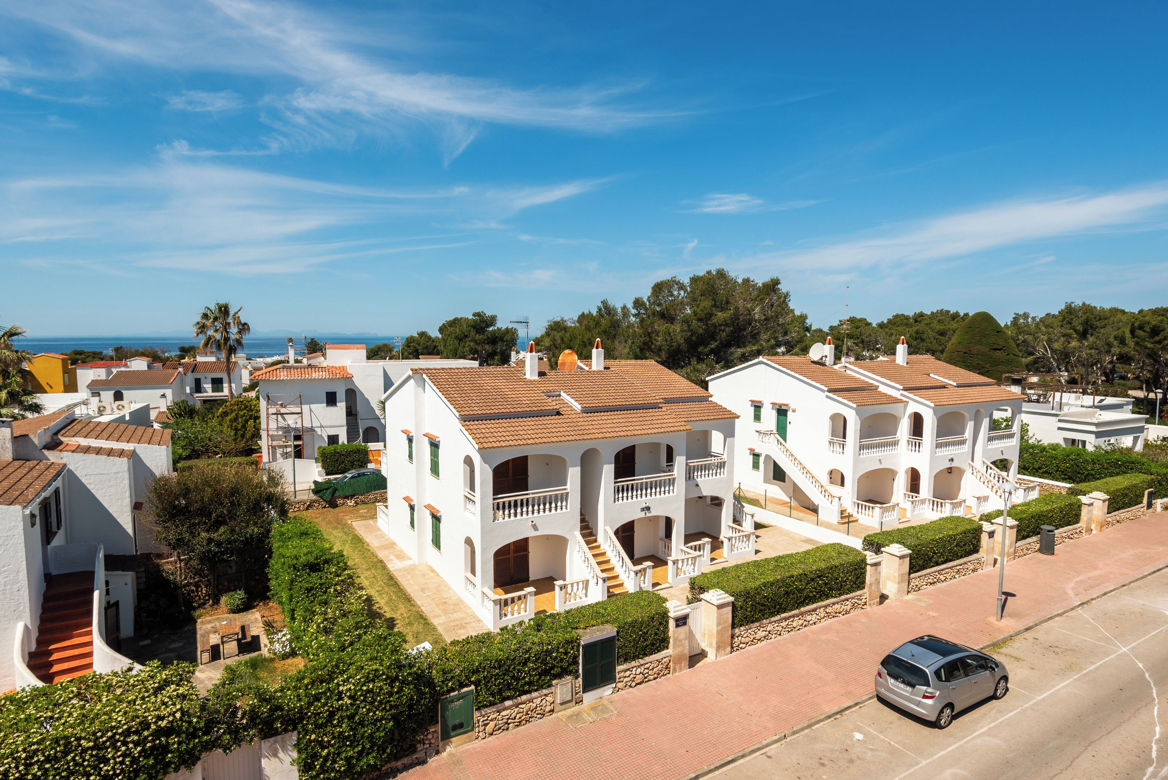 Una zona residencial costera con edificios blancos, cielo despejado y vista al mar.