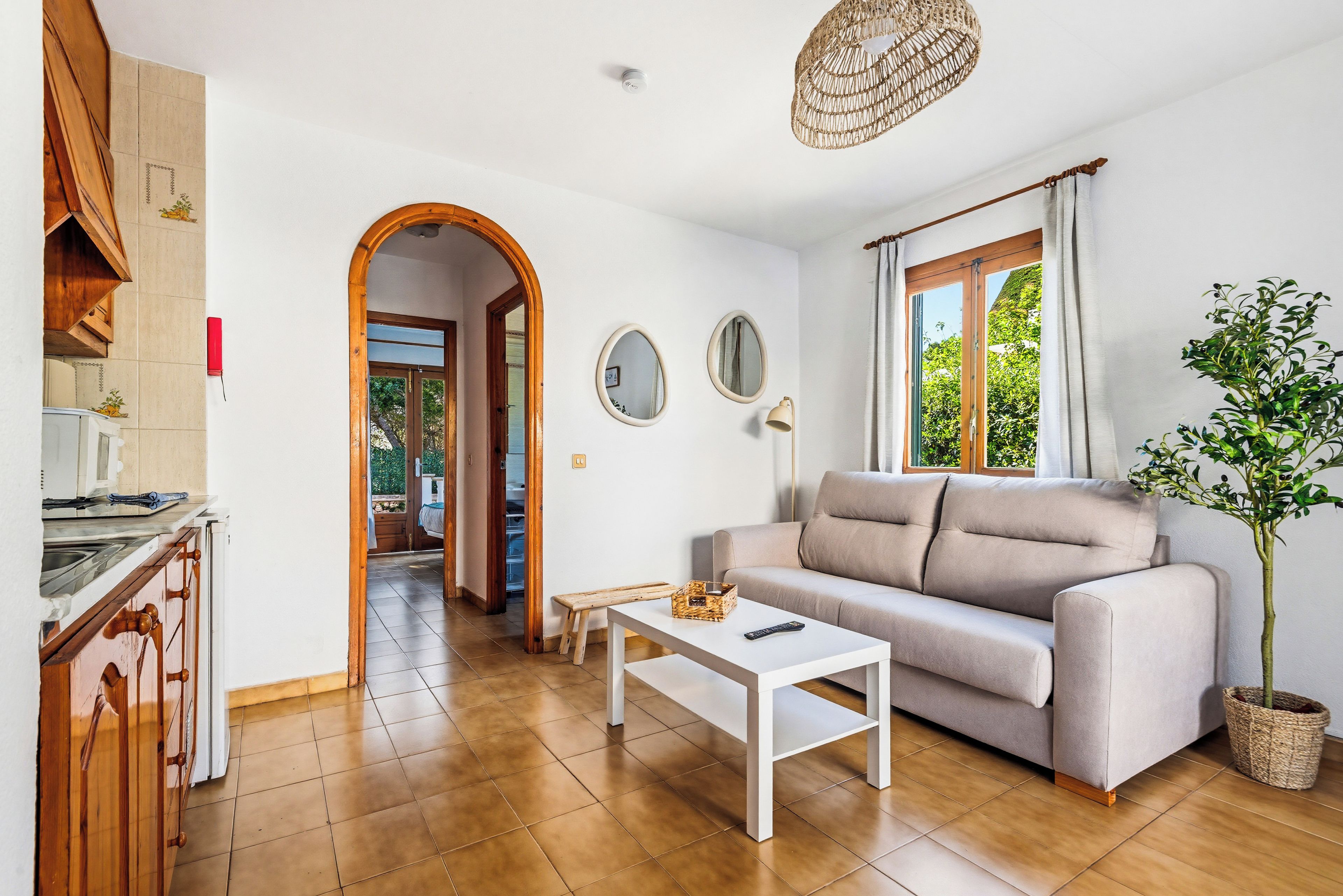 Una sala de estar con un sofá, una mesa de centro, una planta y vistas al exterior a través de una ventana.