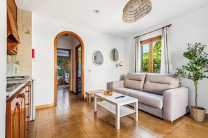 A living room with a sofa, a coffee table, a plant, and a view of the outdoors through a window. - Apartamentos Mar Blanca (Ciutadella de Menorca)