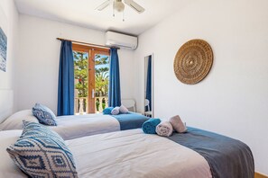 A hotel room with two beds, a balcony with curtains, an air conditioning unit, and a decorative wall piece.