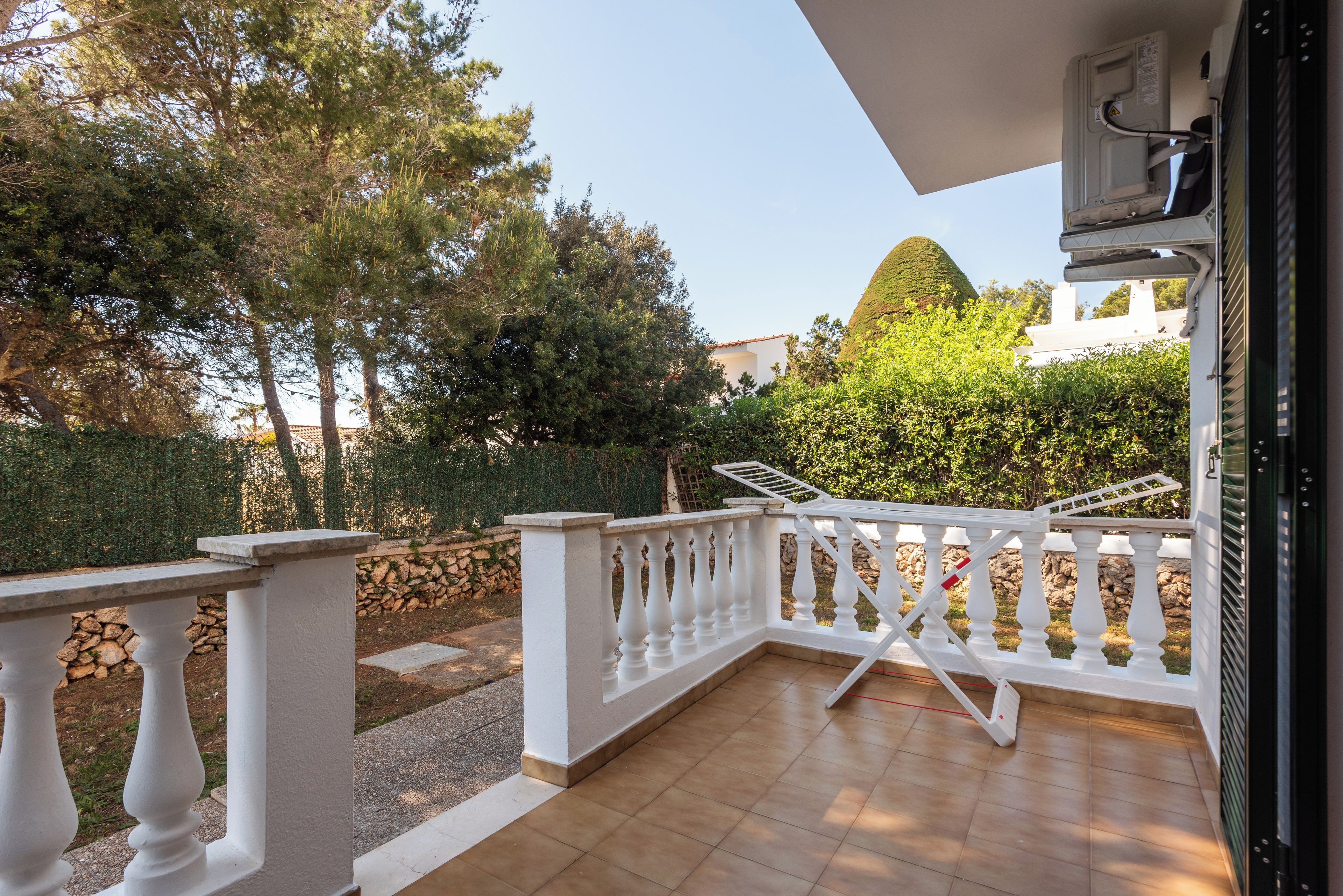 A balcony with a white railing, a stone wall, and a view of trees and a building.