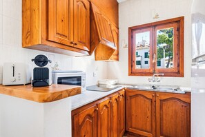 A kitchen with wooden cabinets, a window, a sink, and a toaster. - Apartamentos Mar Blanca (Ciutadella de Menorca)