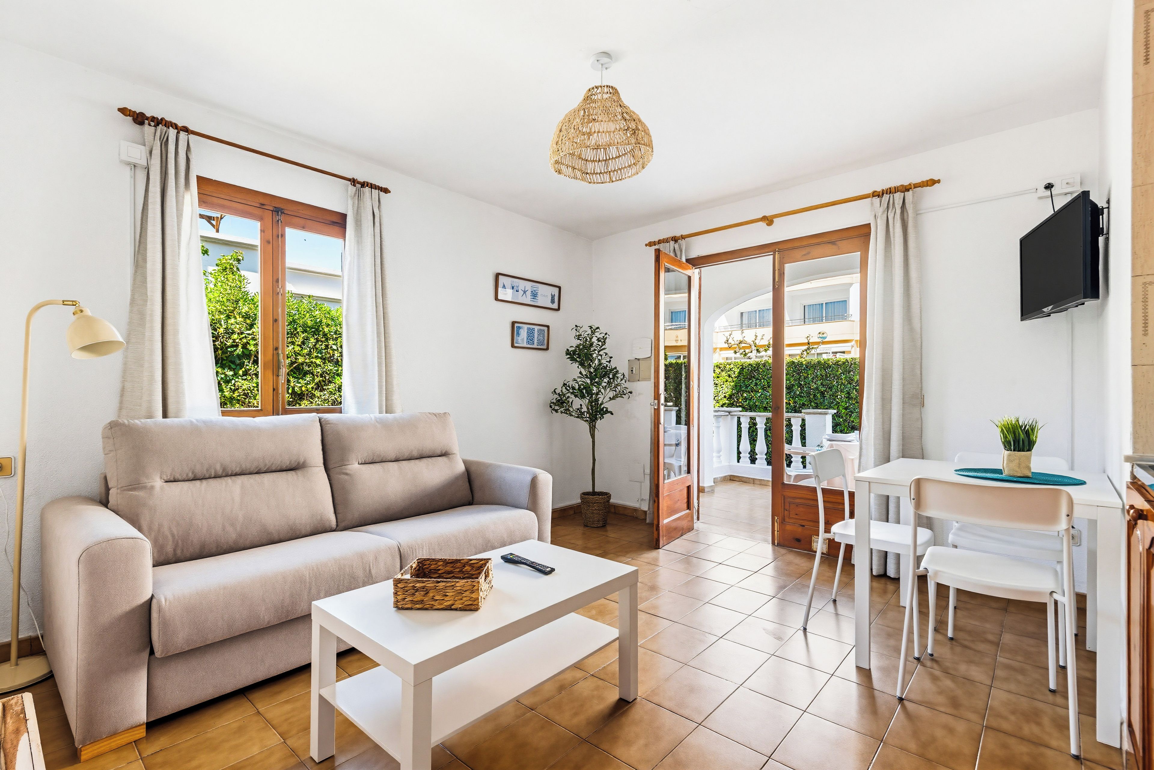 Una sala de estar moderna con sofá, mesa de centro, televisor y un balcón con mobiliario exterior.