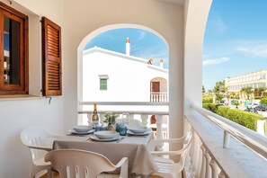 A balcony with a table set for dining, overlooking a building with a white facade and green shutters.