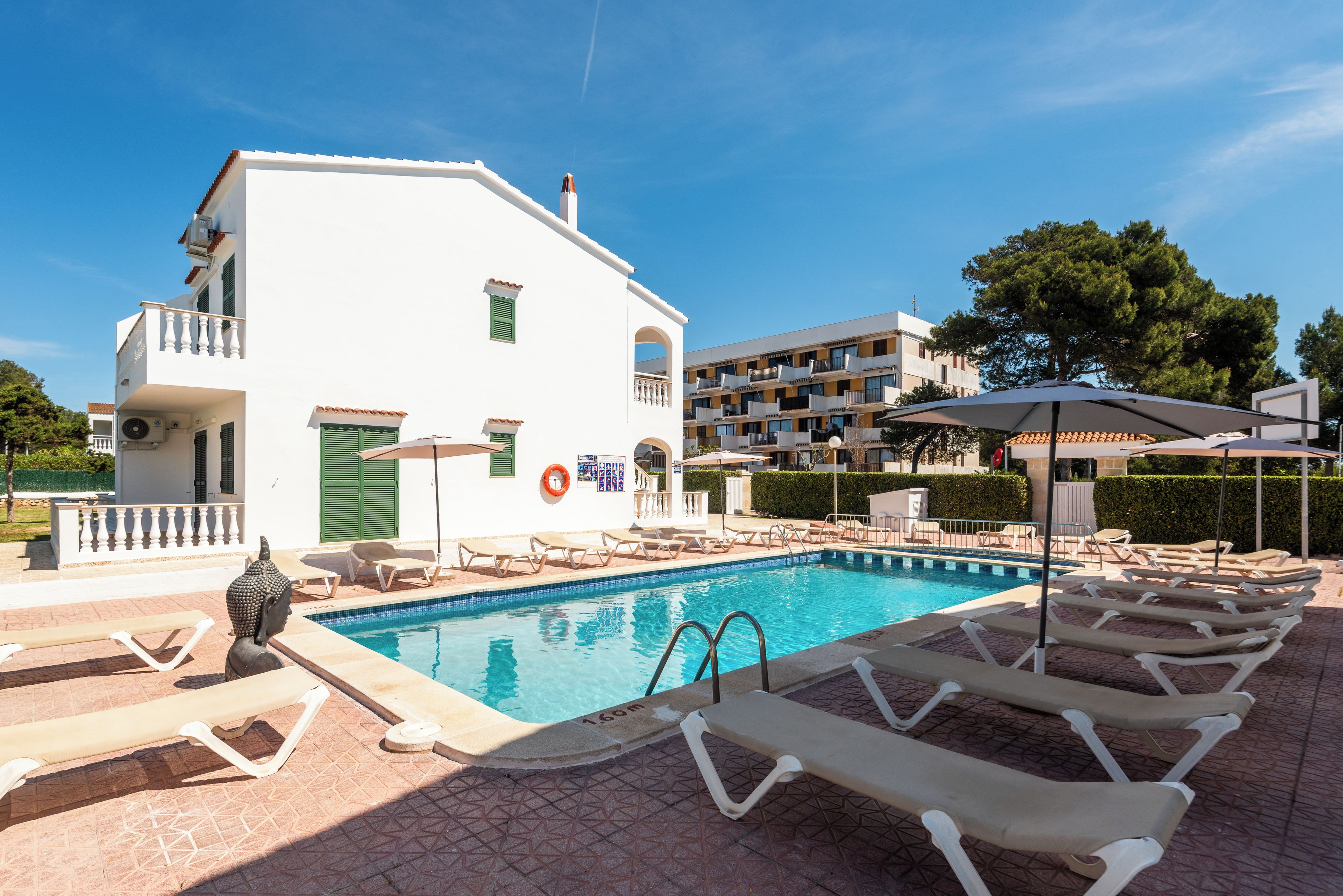 Une piscine avec des chaises longues et un bâtiment blanc doté de balcons.