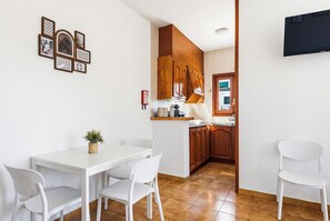 Una cocina compacta con armarios de madera, una encimera blanca y un pequeño comedor con mesa y sillas.